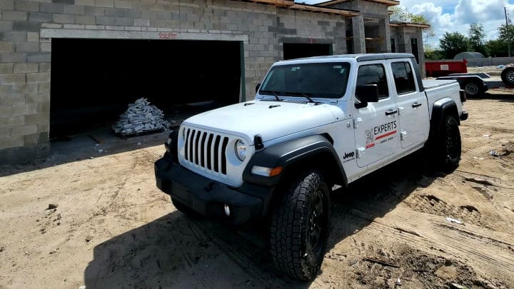 White Jeep Gladiator with garage door service branding parked at a residential construction site with concrete block structure